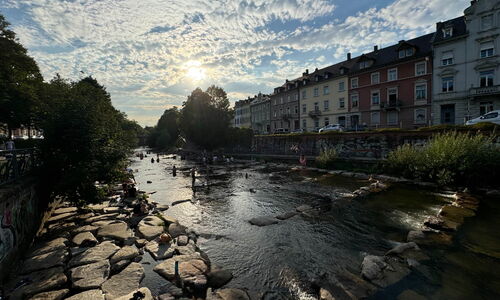 Menschen entspannen an einem sonnigen Sommertag auf den Wasserterrassen der Dreisam in Freiburg