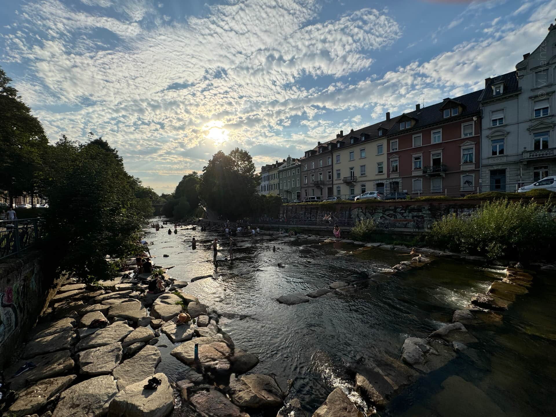 Menschen entspannen an einem sonnigen Sommertag auf den Wasserterrassen der Dreisam in Freiburg
