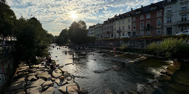Menschen entspannen an einem sonnigen Sommertag auf den Wasserterrassen der Dreisam in Freiburg